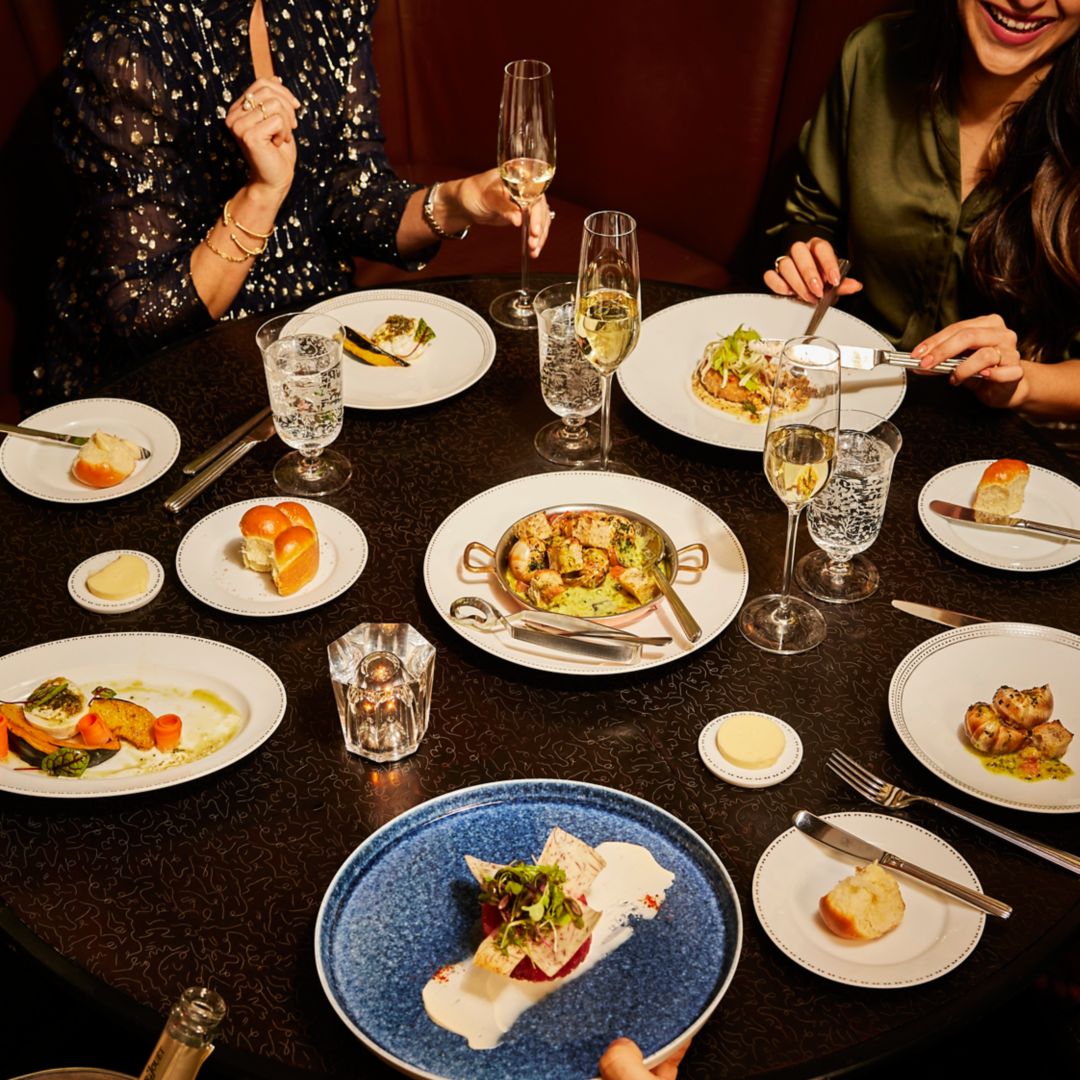 A table with various dishes, glasses of wine, and people enjoying a meal together.